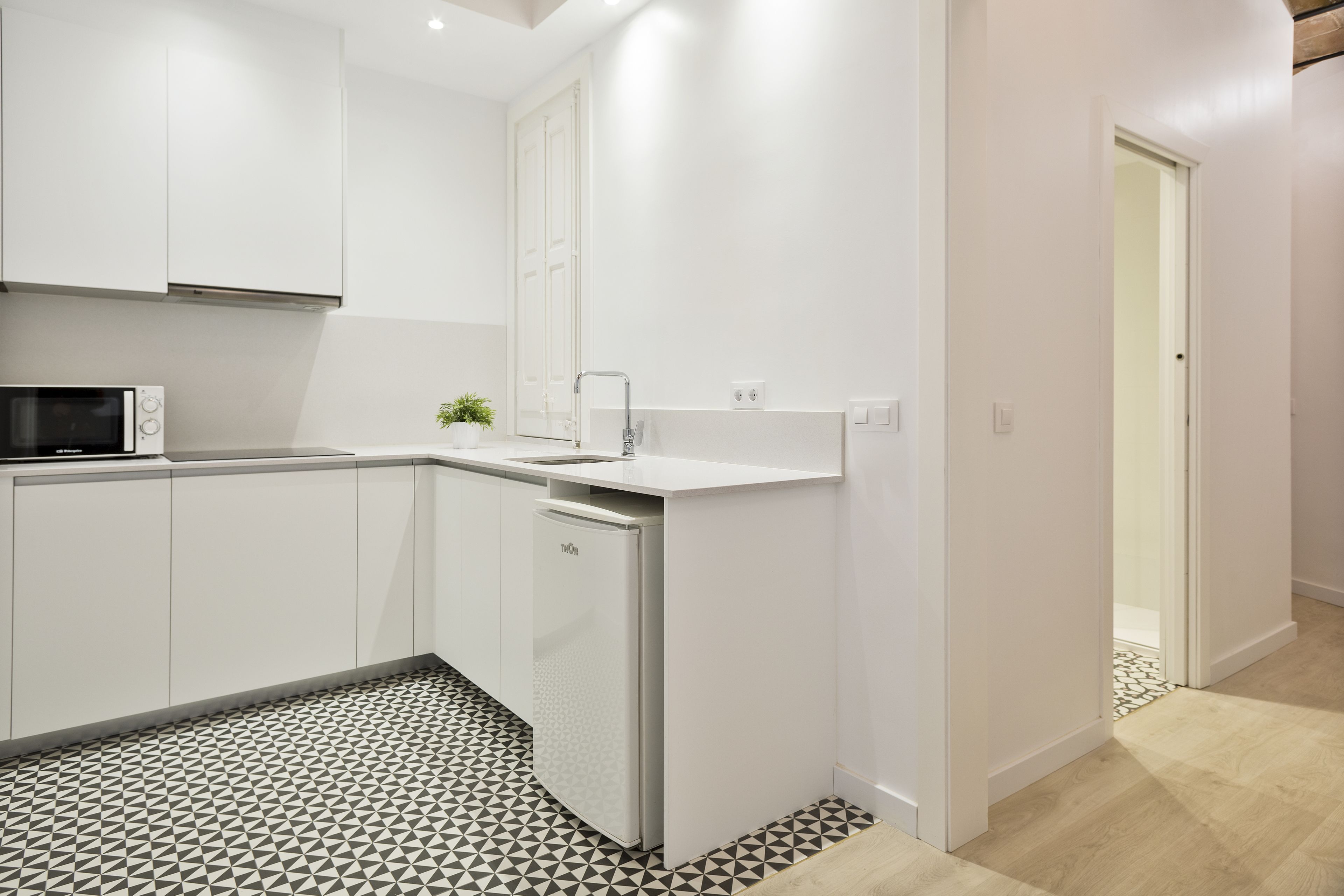 A modern kitchen with white cabinets, a built-in microwave, and a compact refrigerator.