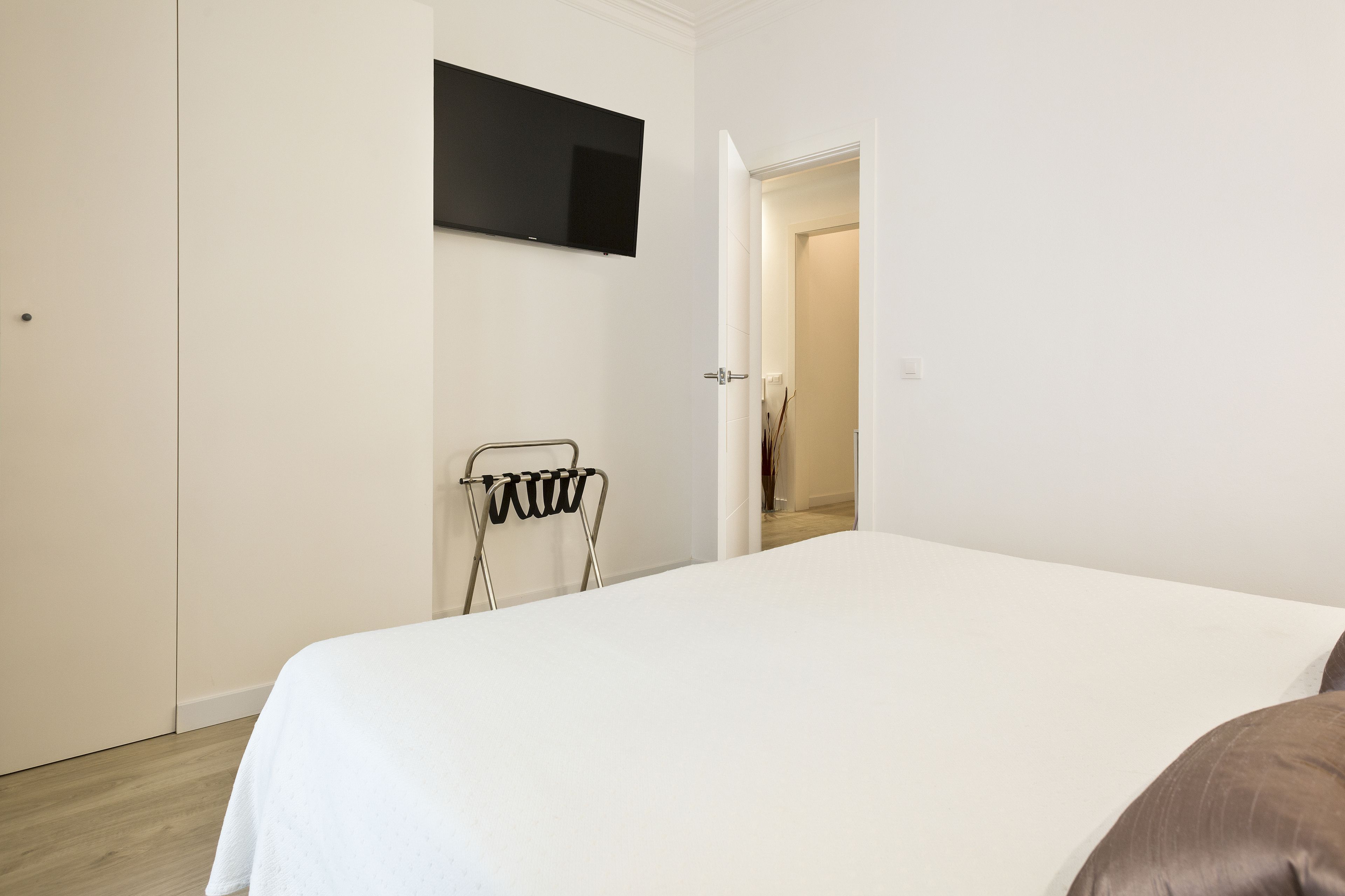 Een slaapkamer met een bed, een aan de muur bevestigde televisie en een deur naar een andere kamer.
