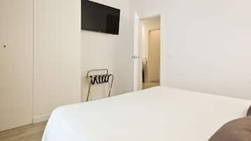 Een slaapkamer met een bed, een aan de muur bevestigde televisie en een deur naar een andere kamer.