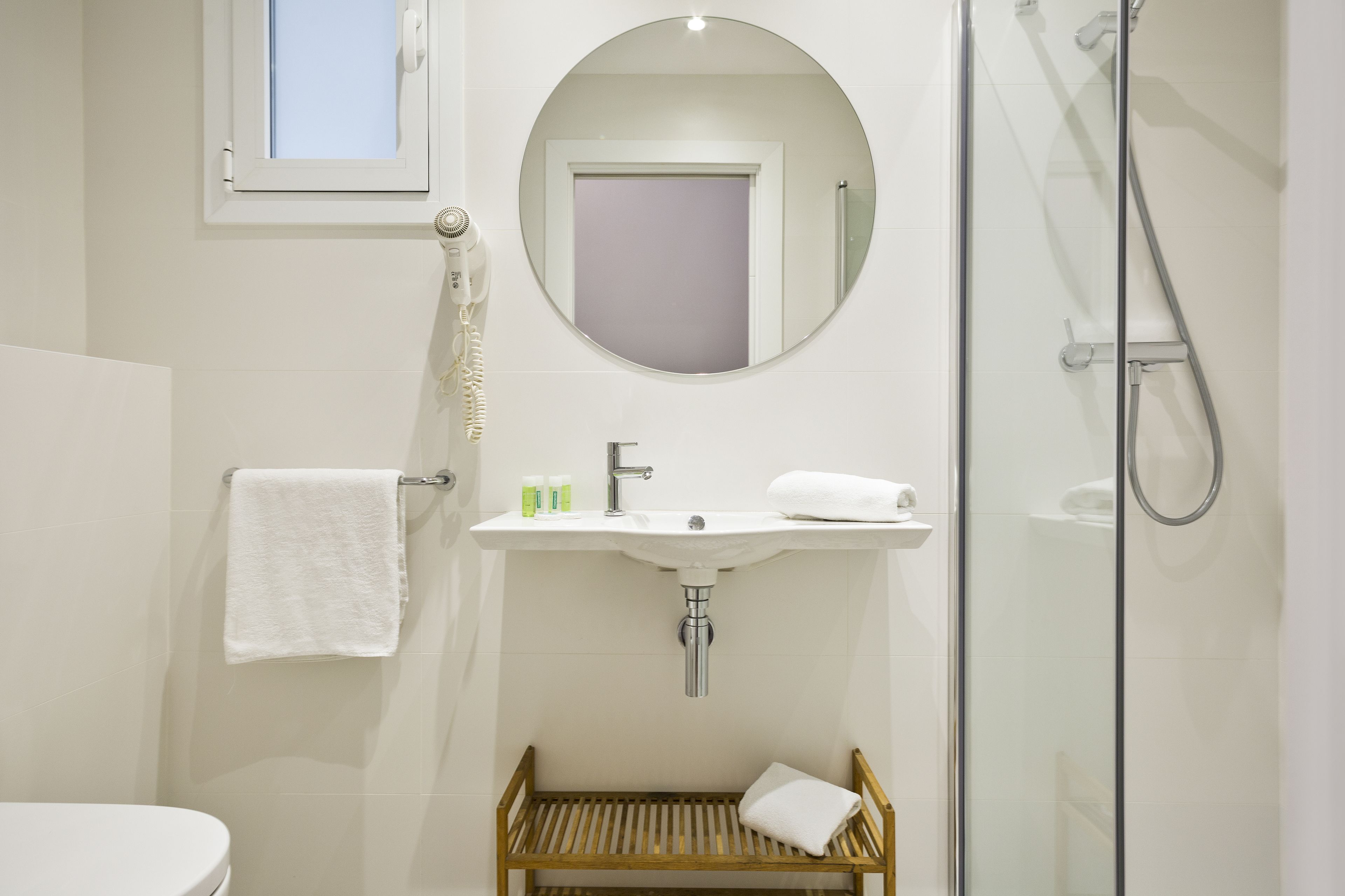 Un baño con lavamanos, espejo, toallero y ducha.