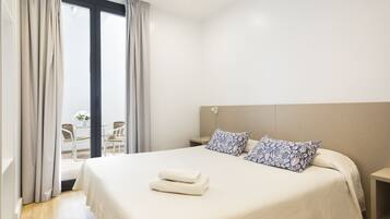 Habitación de hotel con una cama grande, dos almohadas estampadas, una mesita de noche y vistas al exterior a través de un amplio ventanal.
