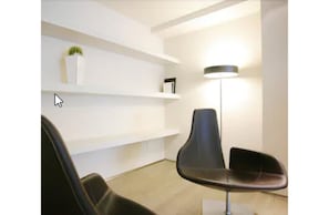 A modern waiting area with a black chair, a floor lamp, and white shelves with a plant and a book. - Art Hotel Udine (Udine)