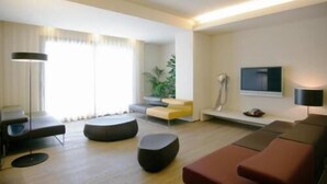 A modern living room with a sofa, ottoman, floor lamp, and a TV mounted on the wall. - Art Hotel Udine (Udine)