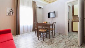 Una habitación con una mesa de comedor, sillas, un televisor y un sofá rojo.