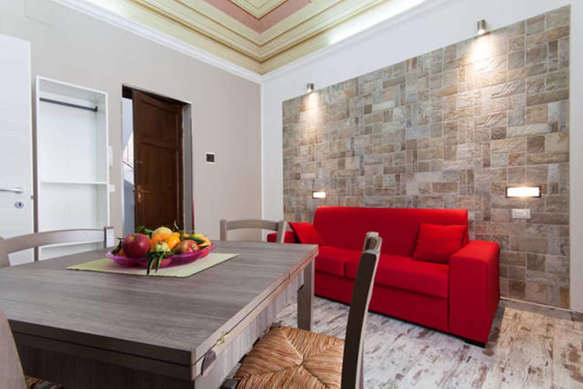 Un coin repas avec une table en bois, un canapé rouge et un mur en pierre.