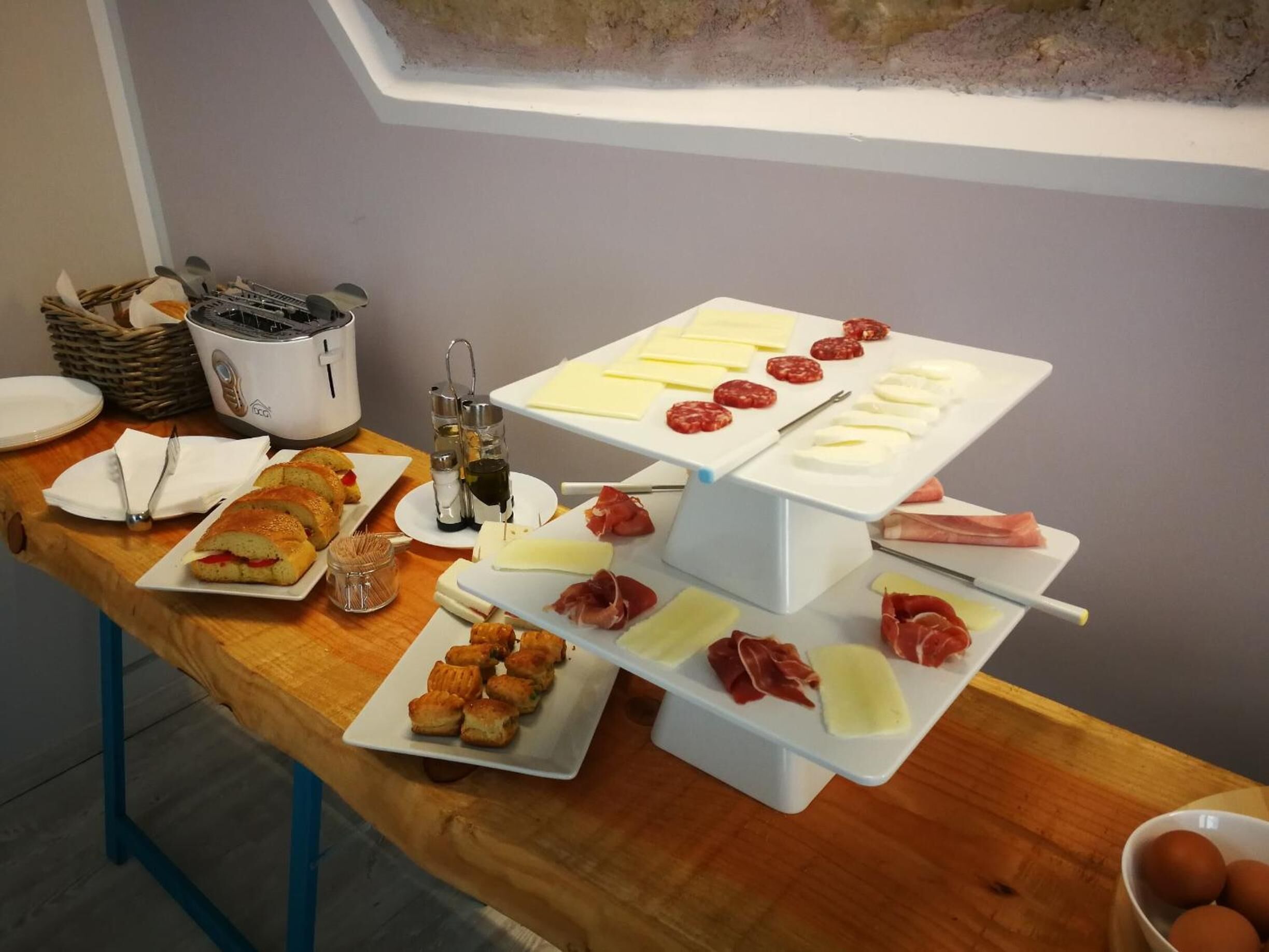 A buffet table with various food items including bread, pastries, cheese, and cured meats.