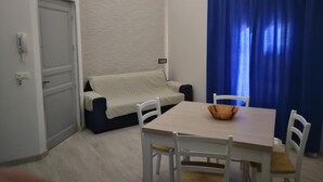 Un espacio habitable pequeño y funcional con sofá, mesa de comedor con sillas, cortina azul y puerta blanca.