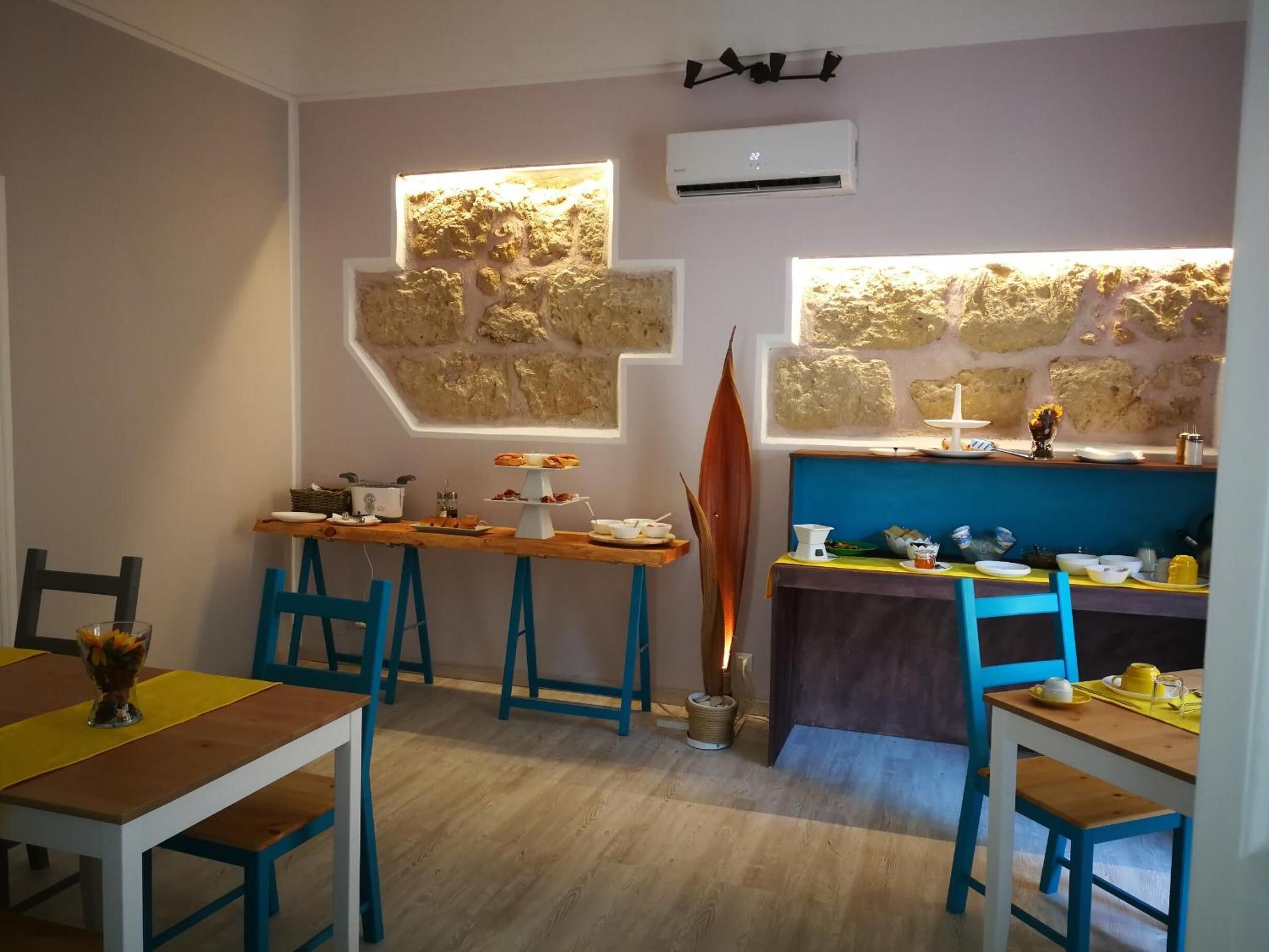 A cozy dining area with a wooden table and blue chairs, a stone wall with built-in lighting, and an air conditioning unit on the ceiling.