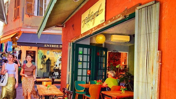 Un café al aire libre con mesas y sillas de madera, un toldo verde y un letrero que dice 'Olivenza'.