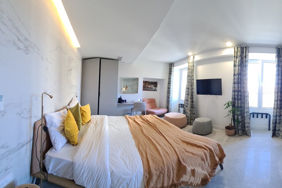 Una habitación de hotel moderna con una cama, un escritorio, una silla, zona de ducha y un ventanal grande.