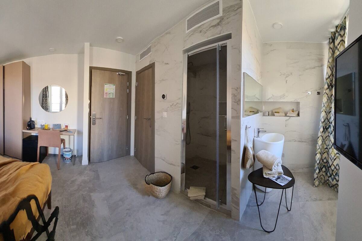 A hotel room with a bed, a desk, a chair, a bathroom with a shower, and a TV.