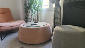 Una sala de estar moderna con una mesa de centro redonda de vidrio, un sillón rosa y un otoman gris.
