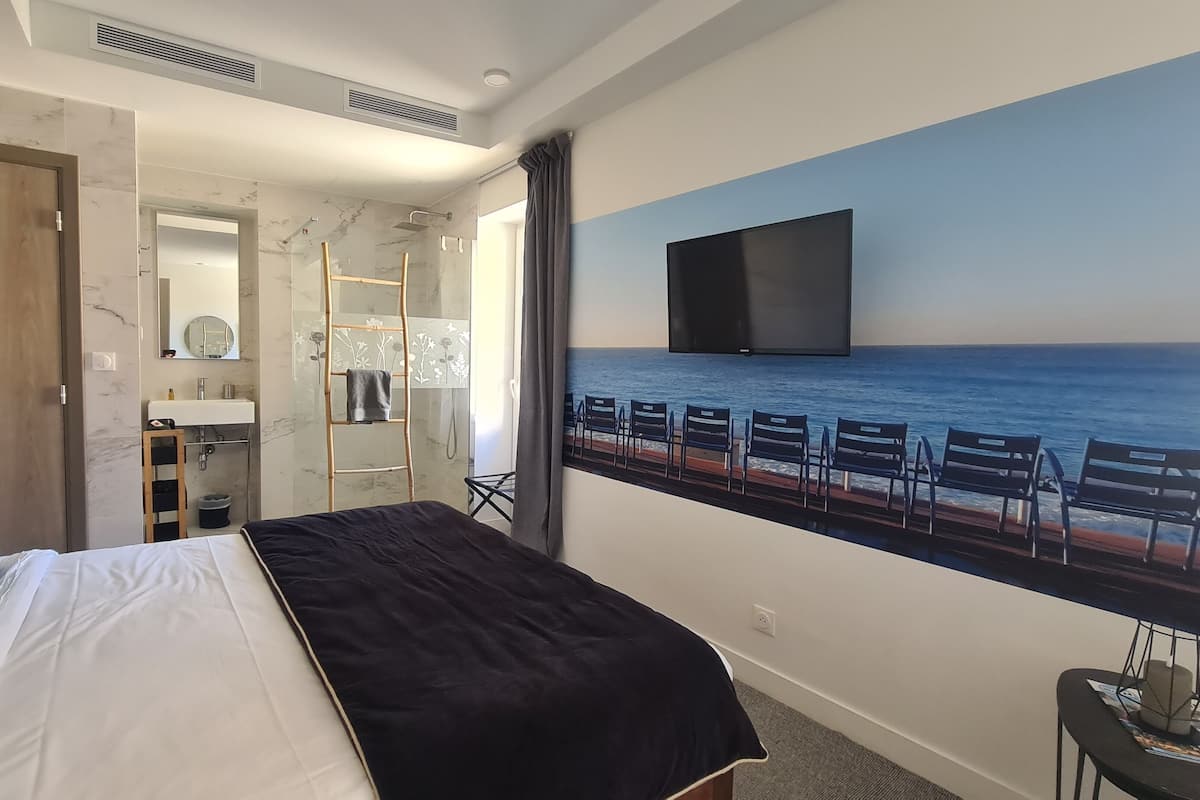 A hotel room with a bed, a bathroom, a TV, and a view of the ocean.