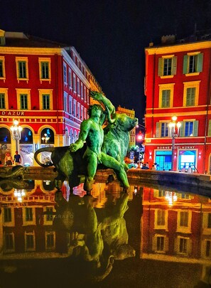 Two figures in a dynamic pose stand in a public square, surrounded by illuminated buildings and a reflective pool.