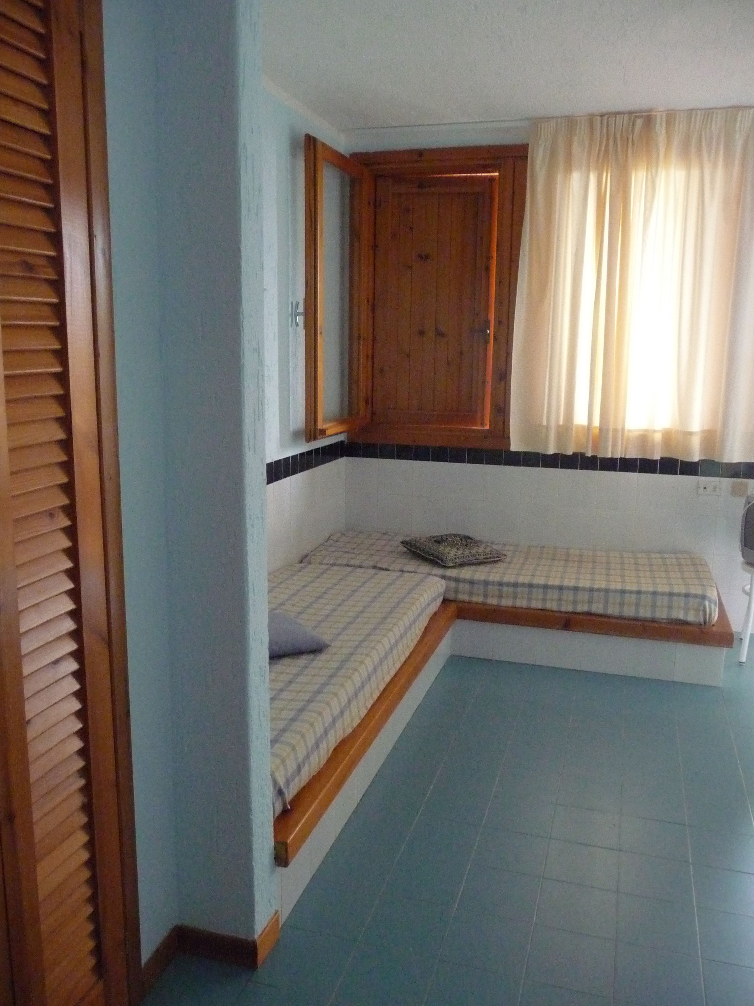 Una stanza piccola e compatta con un letto singolo, un armadietto in legno e una finestra con tende.