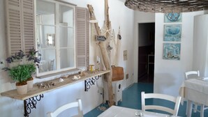 Un comedor con mobiliario blanco, una estantería de madera con objetos decorativos y una pared con motivos náuticos.