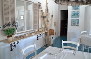 Un comedor con mobiliario blanco, una estantería de madera con objetos decorativos y una pared con motivos náuticos.