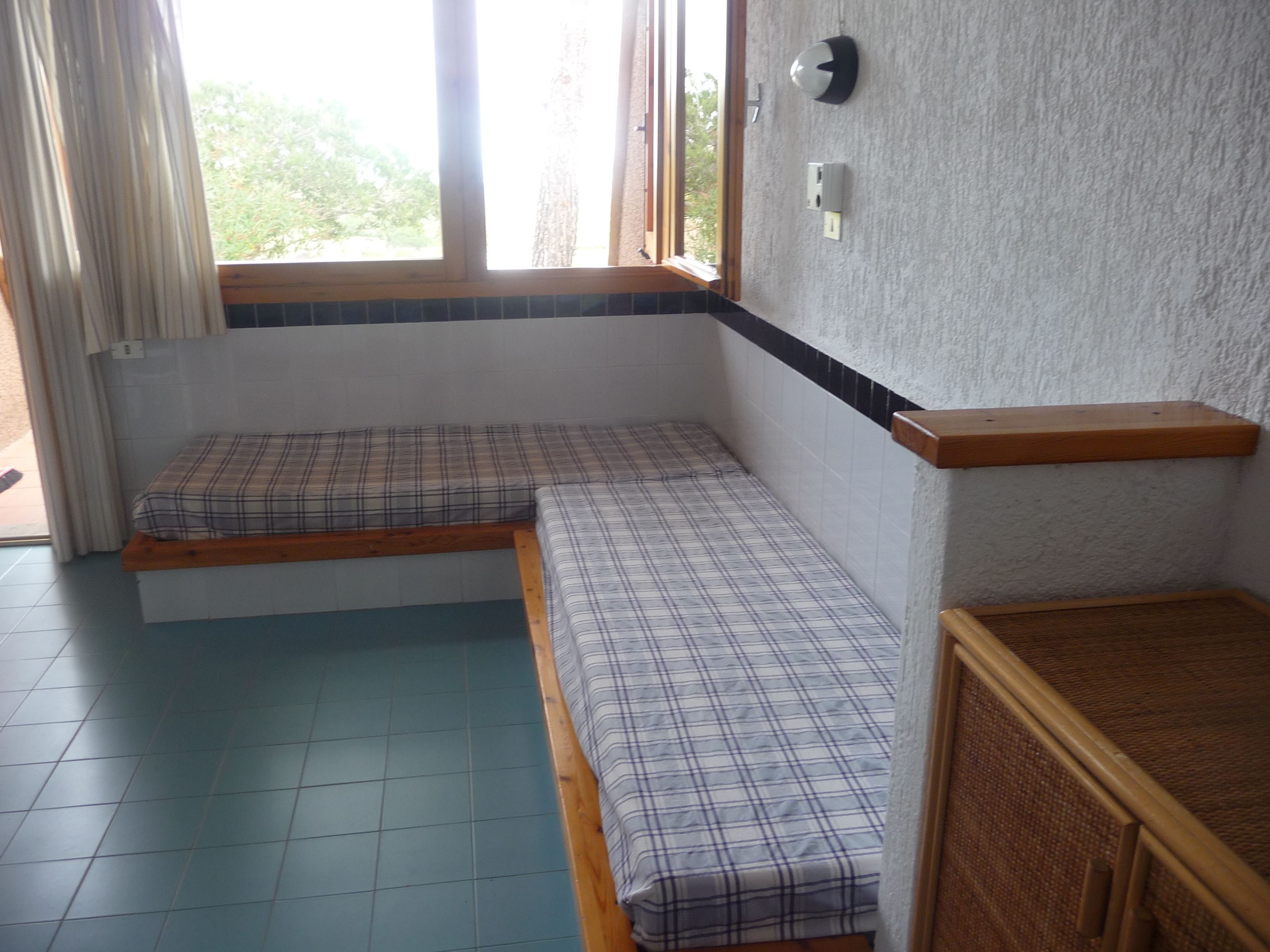 Ein Zimmer mit einem Bett, einer kleinen Holzbank, einem Fenster und einer Wandleuchte.