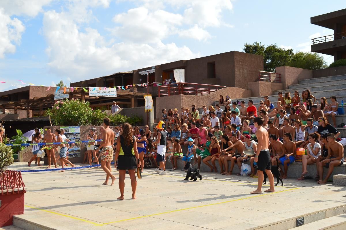 An outdoor sports event with spectators seated on bleachers, a volleyball net, and a crowd of people.
