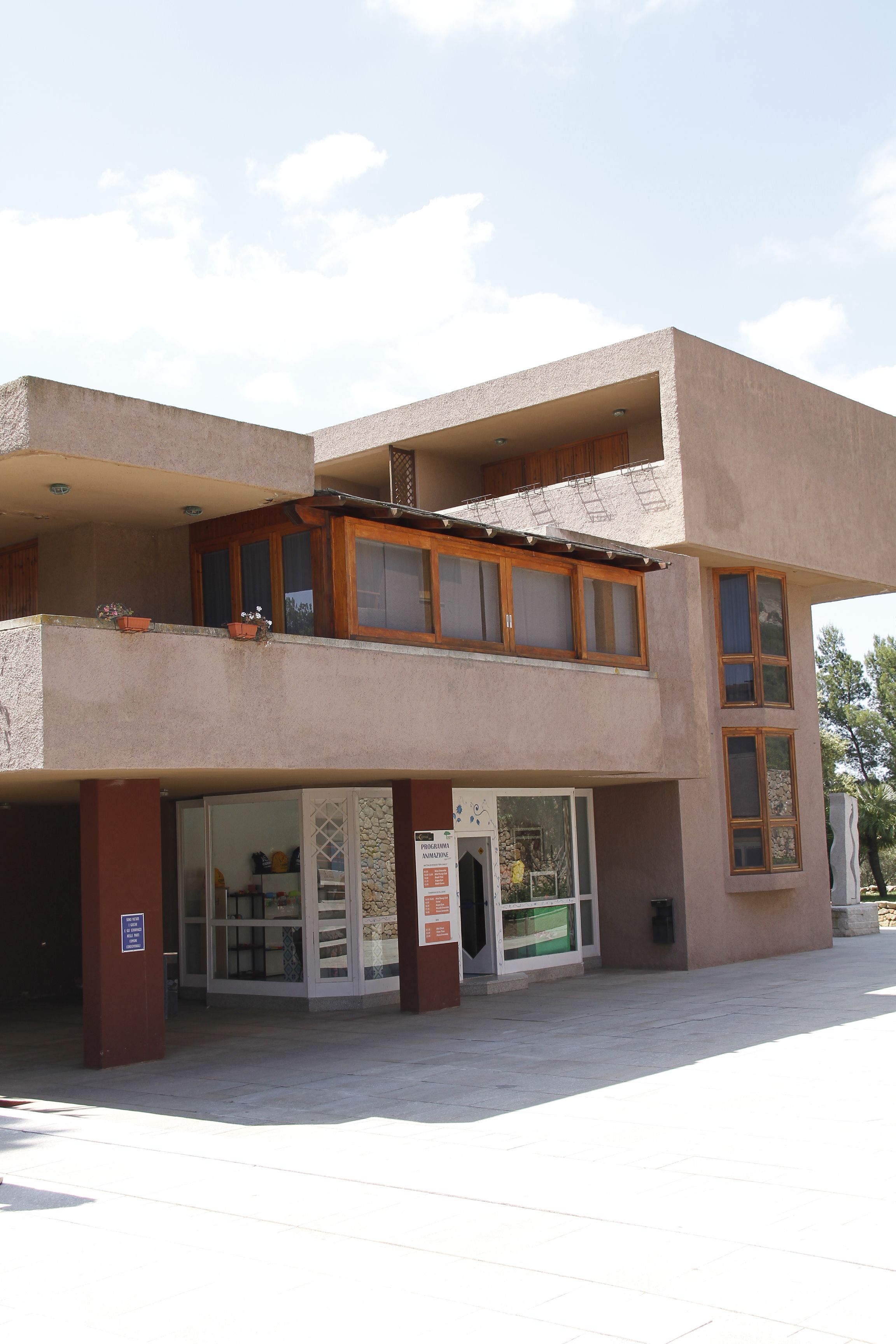 A two-story building with a ground-level entrance, a balcony with wooden railings, and a small shop or cafe area with a glass facade.