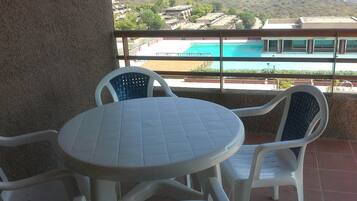 A balcony with a round table and four chairs, overlooking a swimming pool and buildings.