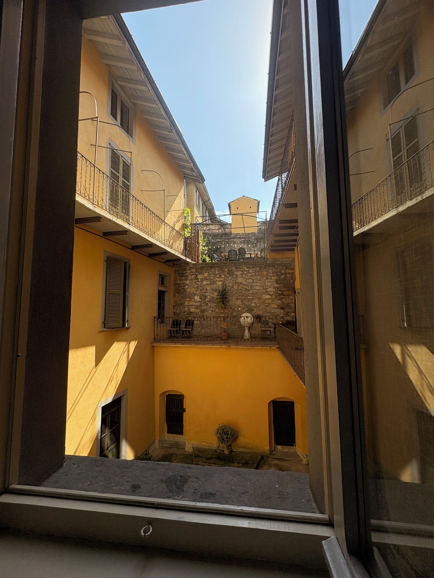 Un patio con un muro de piedra, un pequeño jardín y un edificio con balcón.