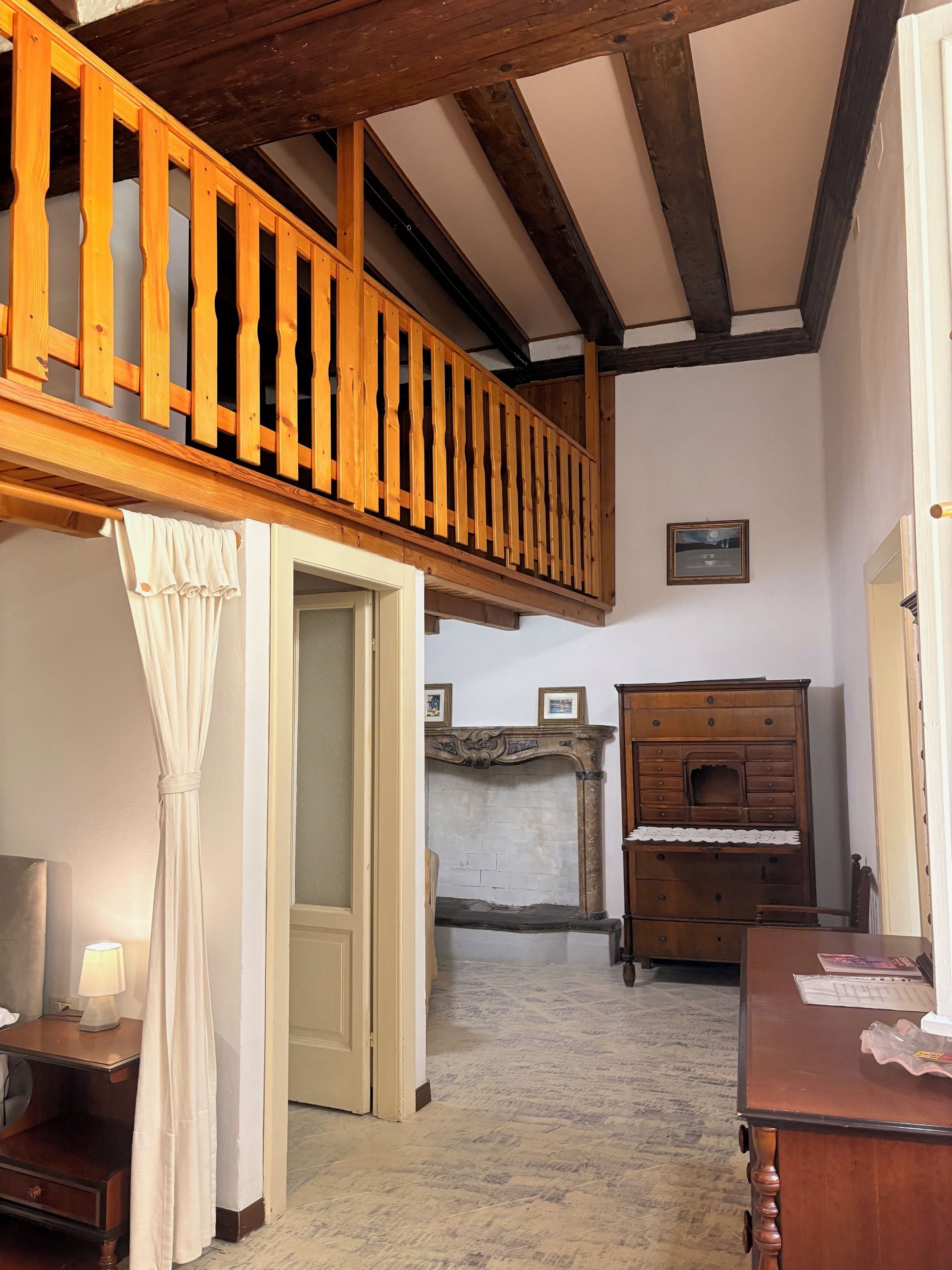 A room with a wooden staircase, a fireplace, a wooden dresser, and a bed with a white curtain.