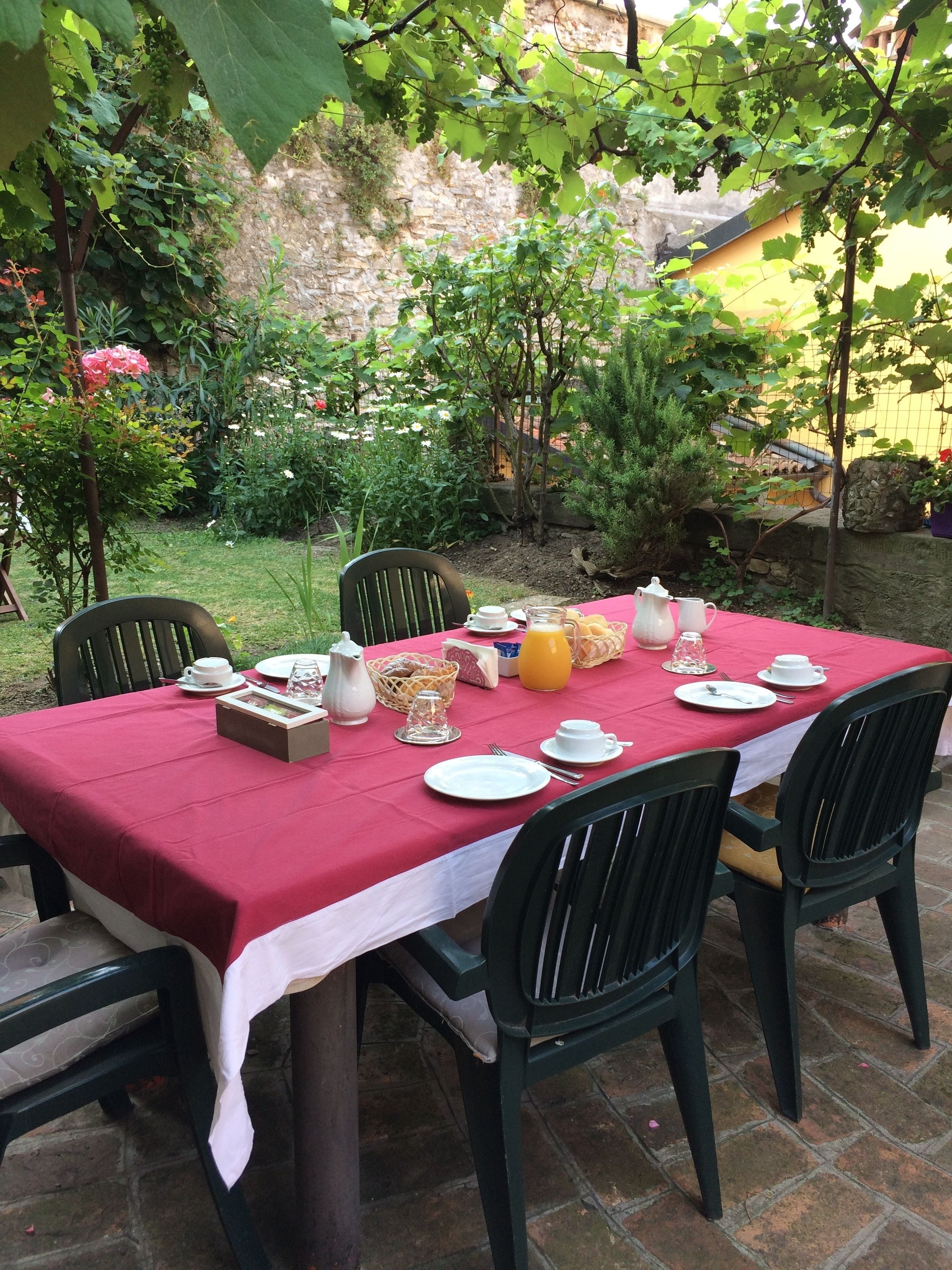 An outdoor dining area with a table set for four, surrounded by greenery and a stone wall.