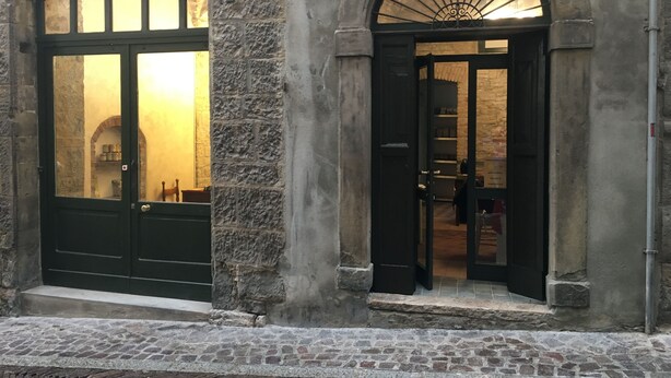 A stone building with two arched doorways, one leading to a room with a large window and the other to a room with a shelf and a door. - Casa Mario Lupo (Bergamo)