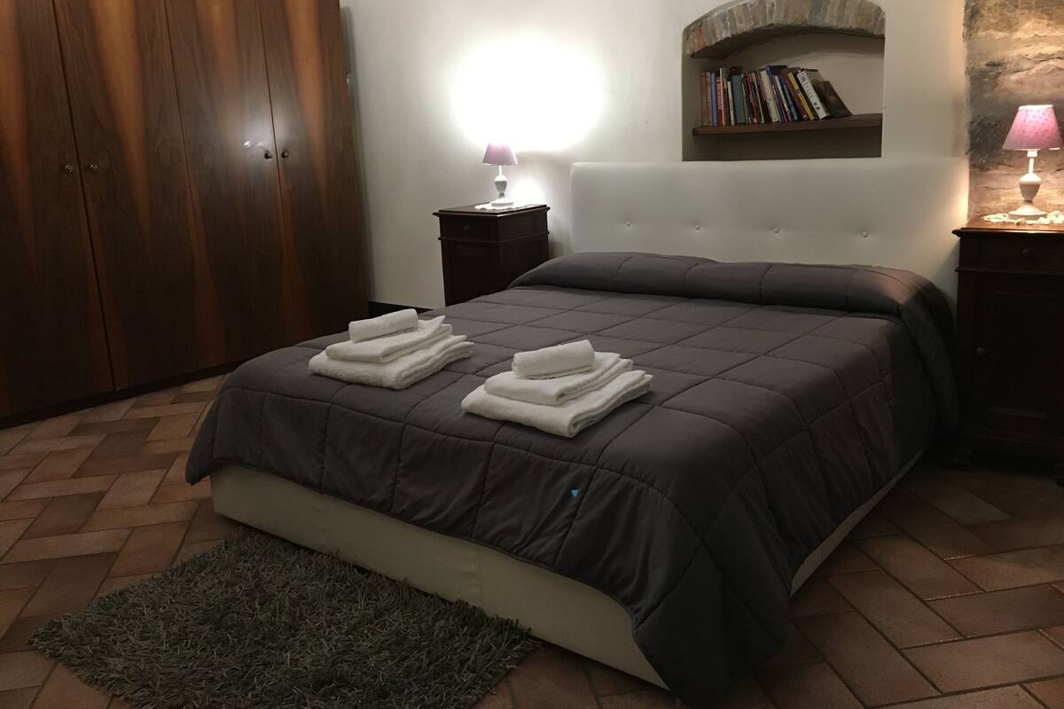 A bedroom with a bed, a wardrobe, a nightstand, a lamp, a bookshelf, and a rug.