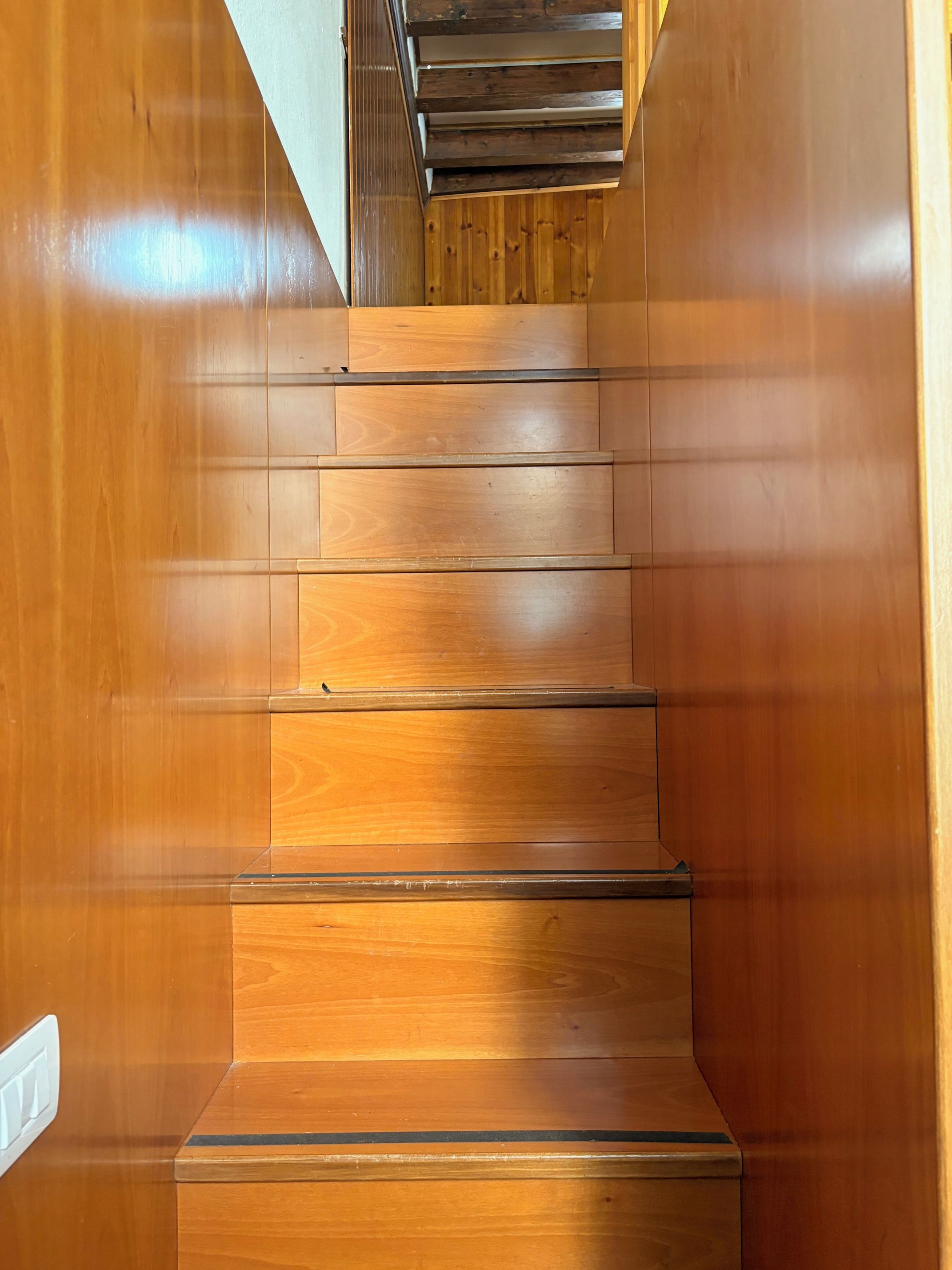 A wooden staircase with a handrail and a light switch on the wall.