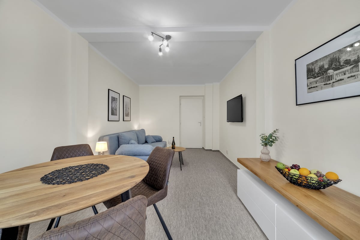 A modern living room with a dining area, a sofa, a coffee table, and a fruit bowl on a wooden shelf.