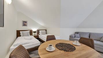 A modern hotel room with a round wooden table, two beds, a gray sofa, and a picture on the wall.