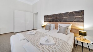 Una habitación de hotel moderna con una cama grande, cabecera de madera, pared con estampado, mesita de noche con lámpara y un armario.