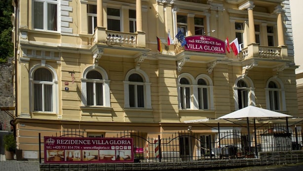 Un edificio de varios pisos con balcones, un letrero que dice "REZIDENCE VILLA GLORIA" y banderas.