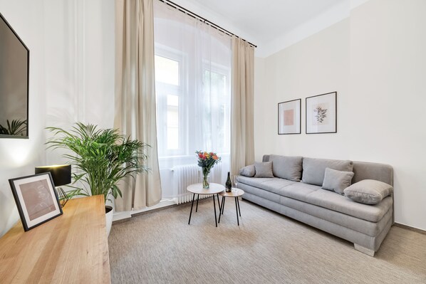 A modern living room with a grey sofa, a round coffee table, a potted plant, and a framed picture on a wooden side table.