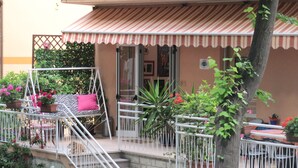 A balcony with a striped awning, potted plants, and a swing chair. - Hotel Villa Elia (Rimini)