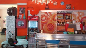 A bar area with a red and orange wall, a vintage motorcycle, and a refrigerator stocked with beverages. - Hotel Villa Elia (Rimini)