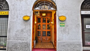 A hotel entrance with a wooden door, a red carpet, and signs indicating the hotel name and location. - Hotel Vecchia Milano (Milan)
