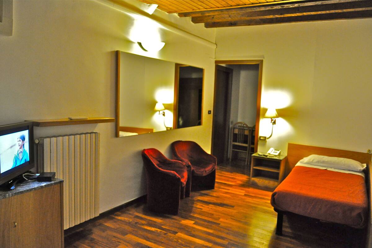 A hotel room with a bed, a TV, two chairs, and a desk with a lamp.