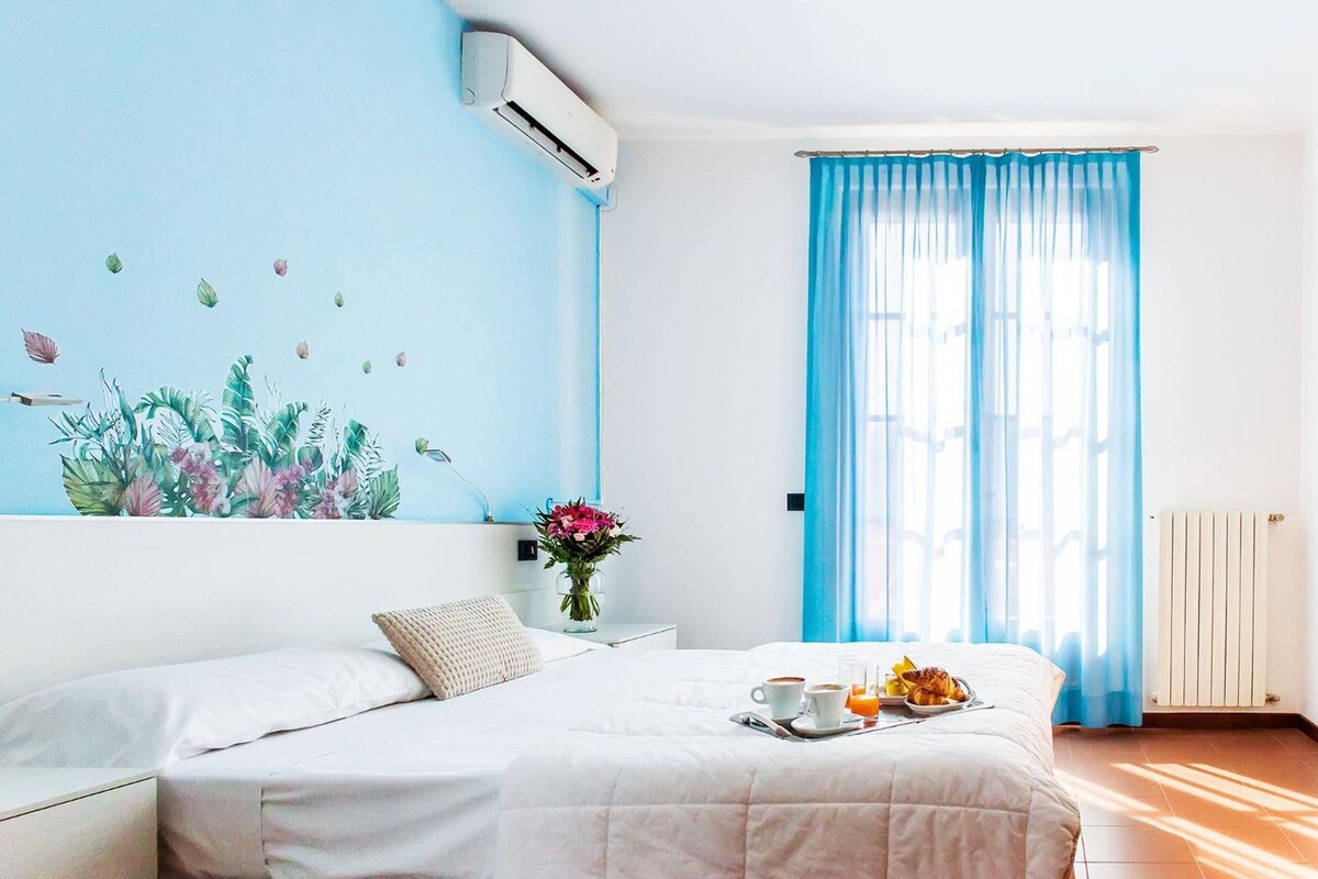 Habitación de hotel con cama, aire acondicionado de pared, ventana con cortinas azules y bandeja de desayuno sobre la cama.