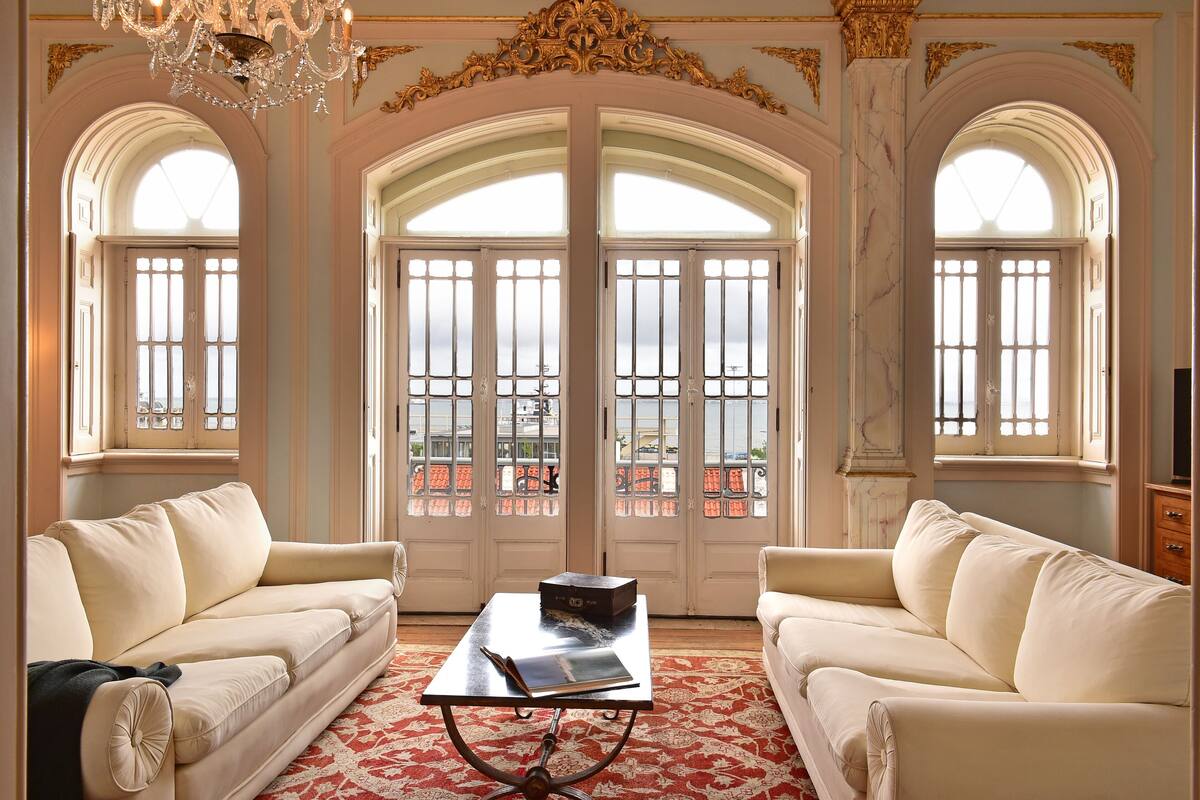 A luxurious room with two cream-colored sofas facing a large arched window with a view of a cityscape.