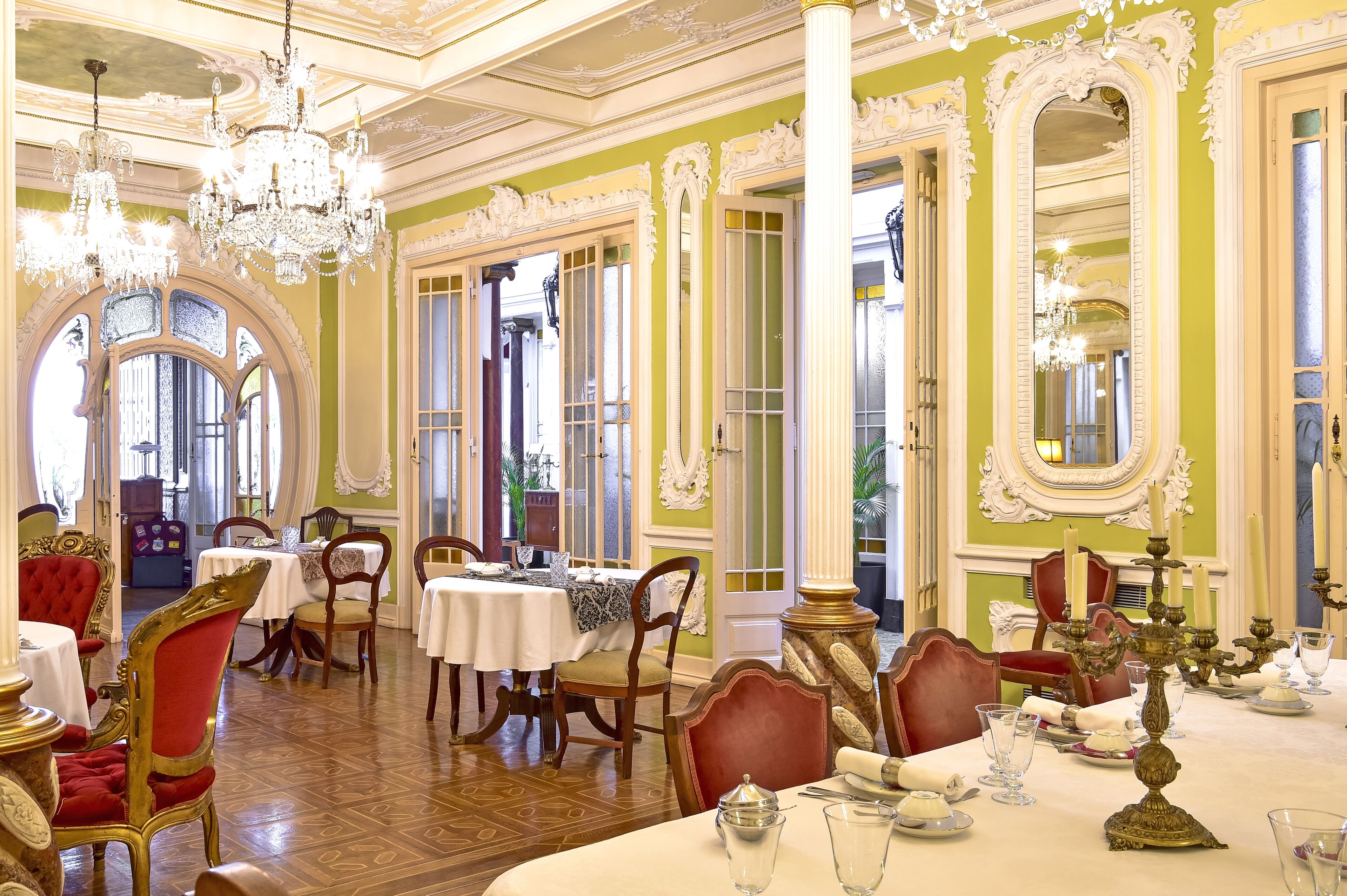 A dining area with ornate chandeliers, red upholstered chairs, and white tablecloths.