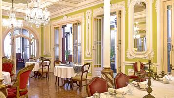 A dining area with ornate chandeliers, red upholstered chairs, and white tablecloths.