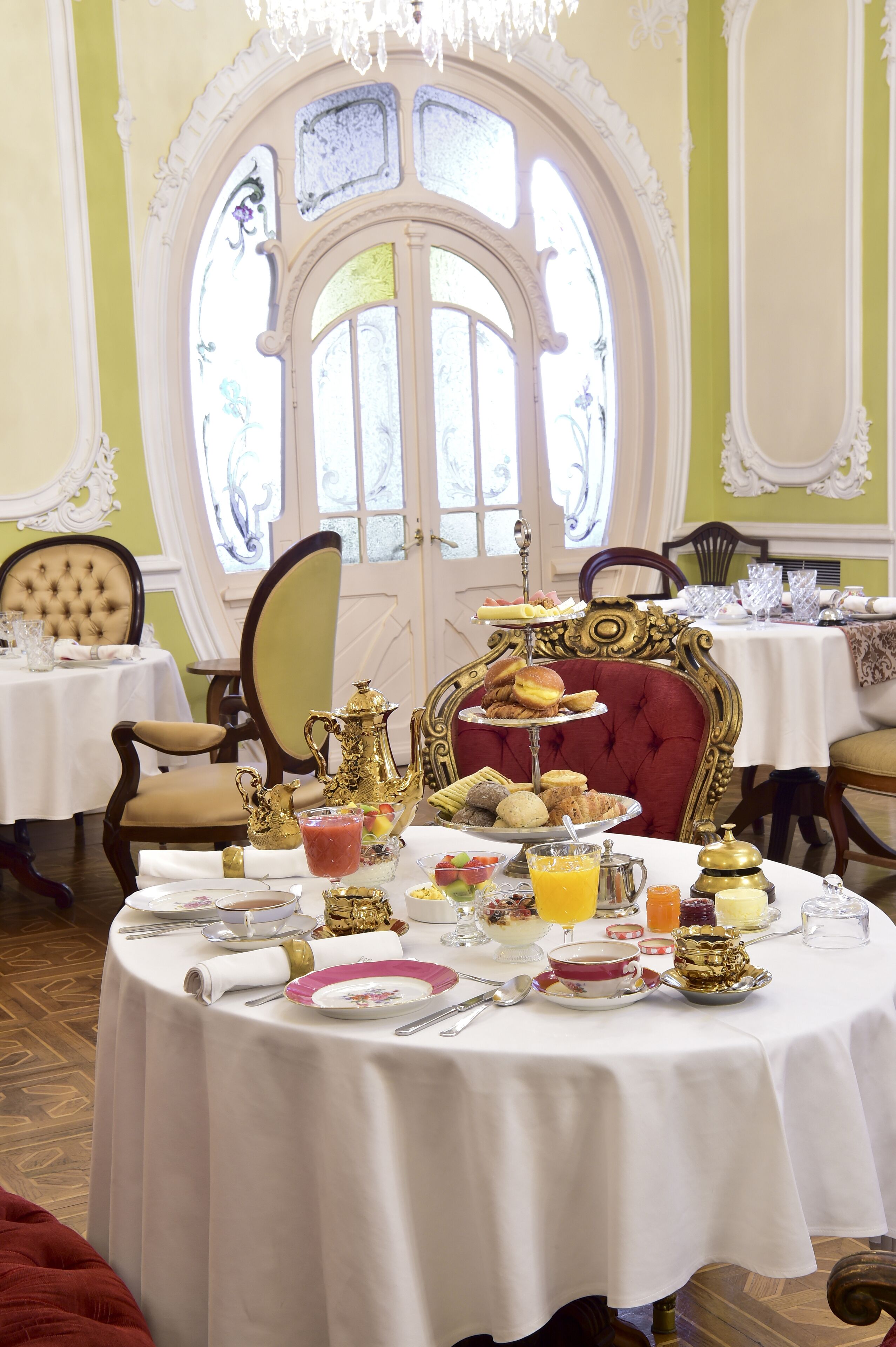 A dining room with a large ornate window, a table set with breakfast, and classic furniture.