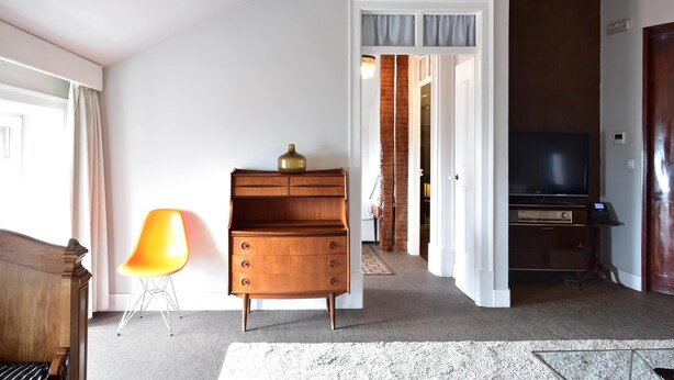 Ein Zimmer mit einem Holzkapuzen, einem modernen orangefarbenen Sessel, einem Fernseher und einer Tür zu einem weiteren Raum.