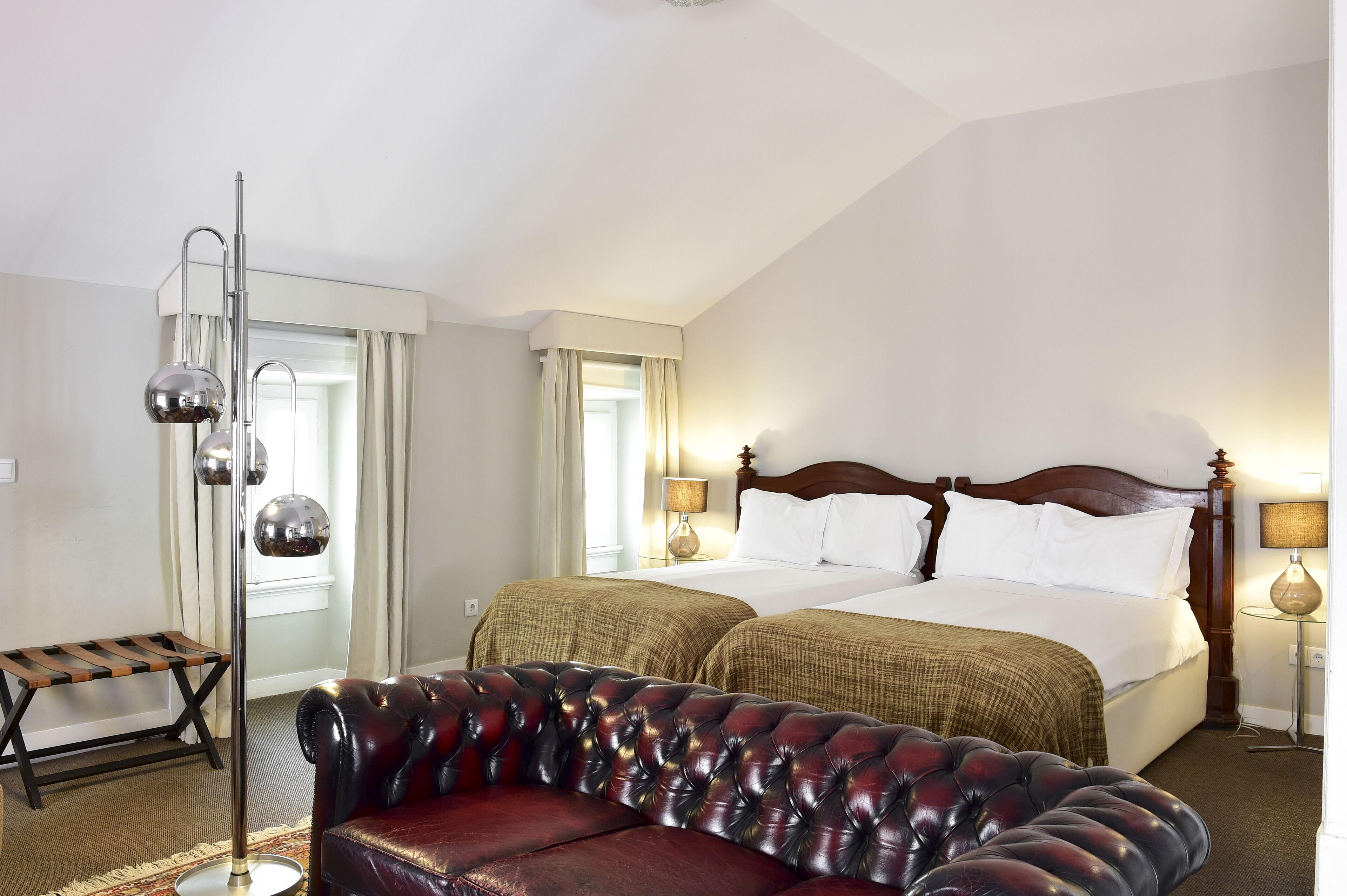 Una habitación de hotel con una cama grande, un sofá de cuero, una lámpara de pie y un banco.