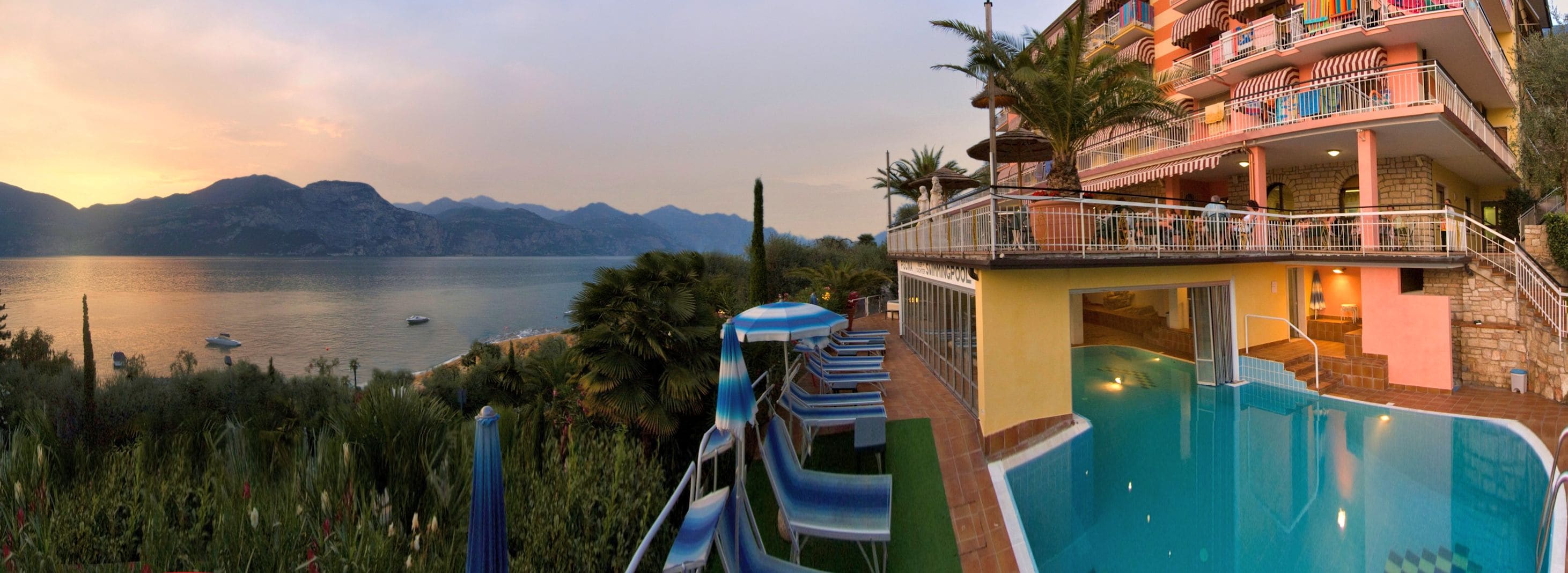 A pool area with a view of a lake and mountains, a slide, and a building with balconies.