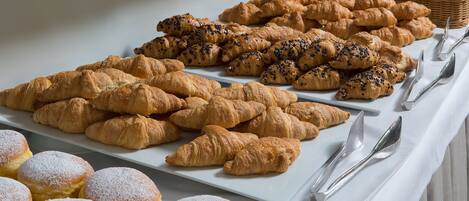 A buffet table with various pastries and bread, including croissants and muffins, arranged neatly on white plates.