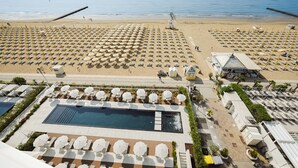 Un complexe hôtelier de bord de mer avec des rangées de chaises longues et de parasols, une piscine et une vue sur l’océan.